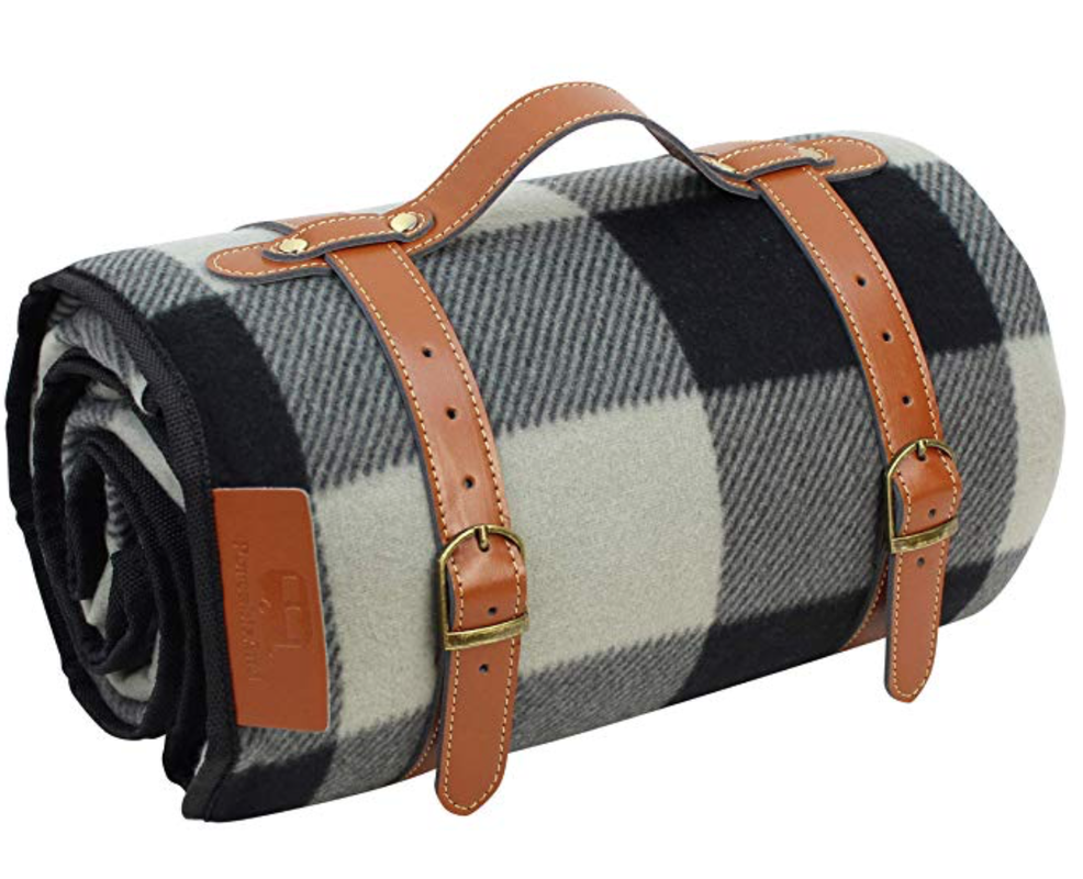 Plaid picnic blanket rolled up and held by leather straps to carry easily